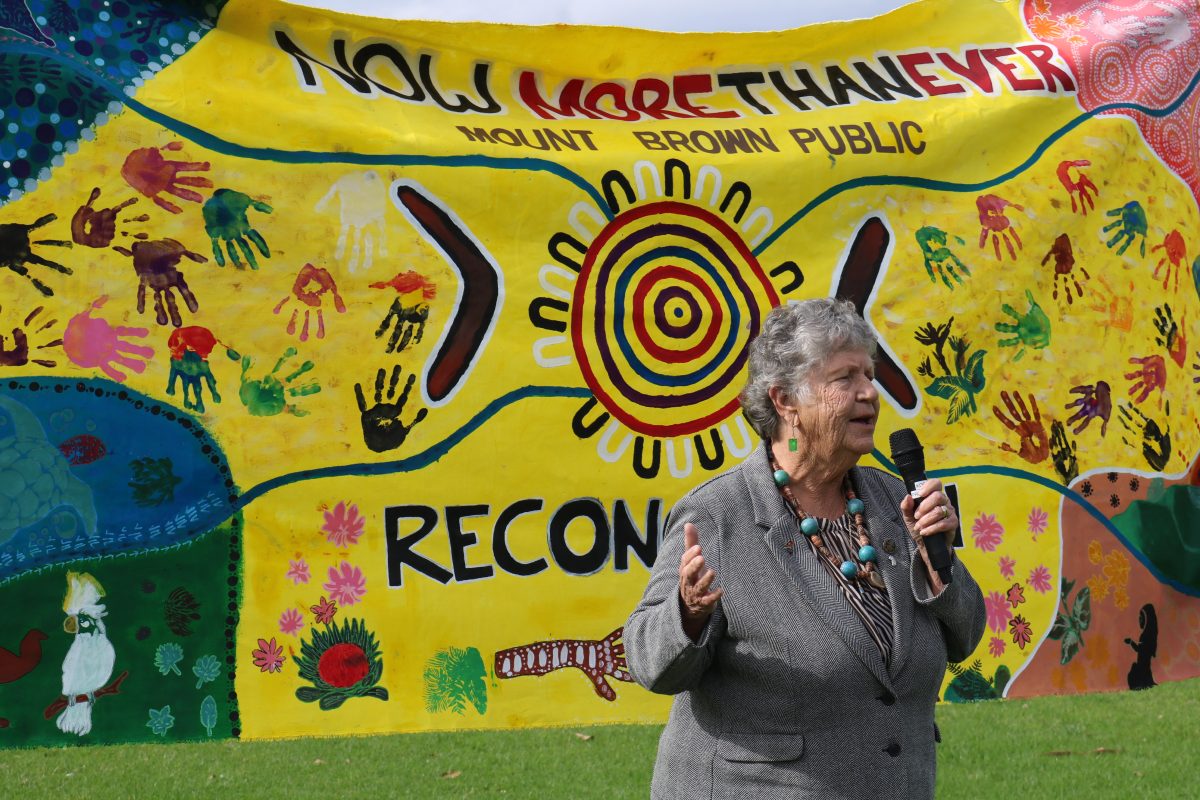 Woman with a microphone in front of a banner.