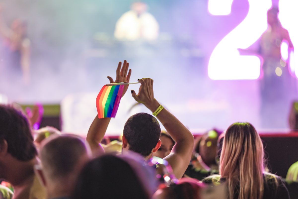 In a crowd one person raises a rainbow flag