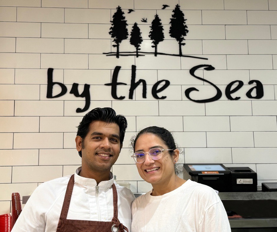 Two people in front of By The Sea restaurant sign.