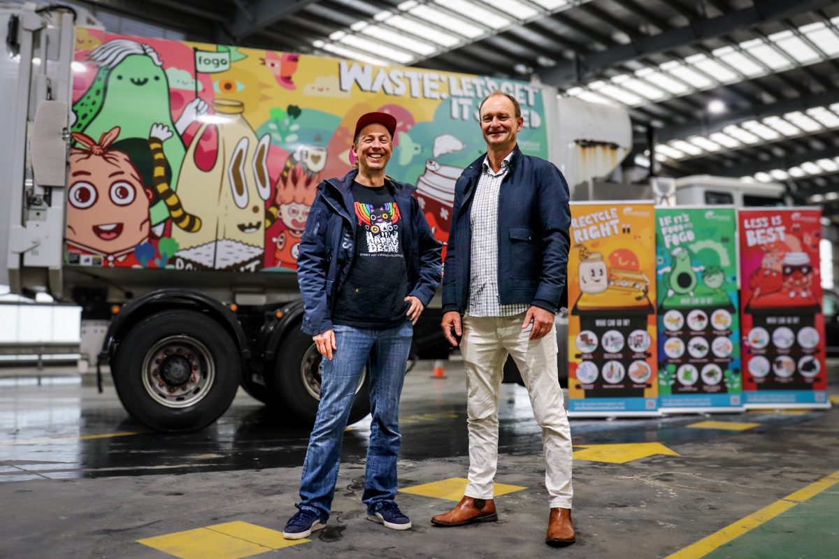 Two men standing in front of painted garbage truck