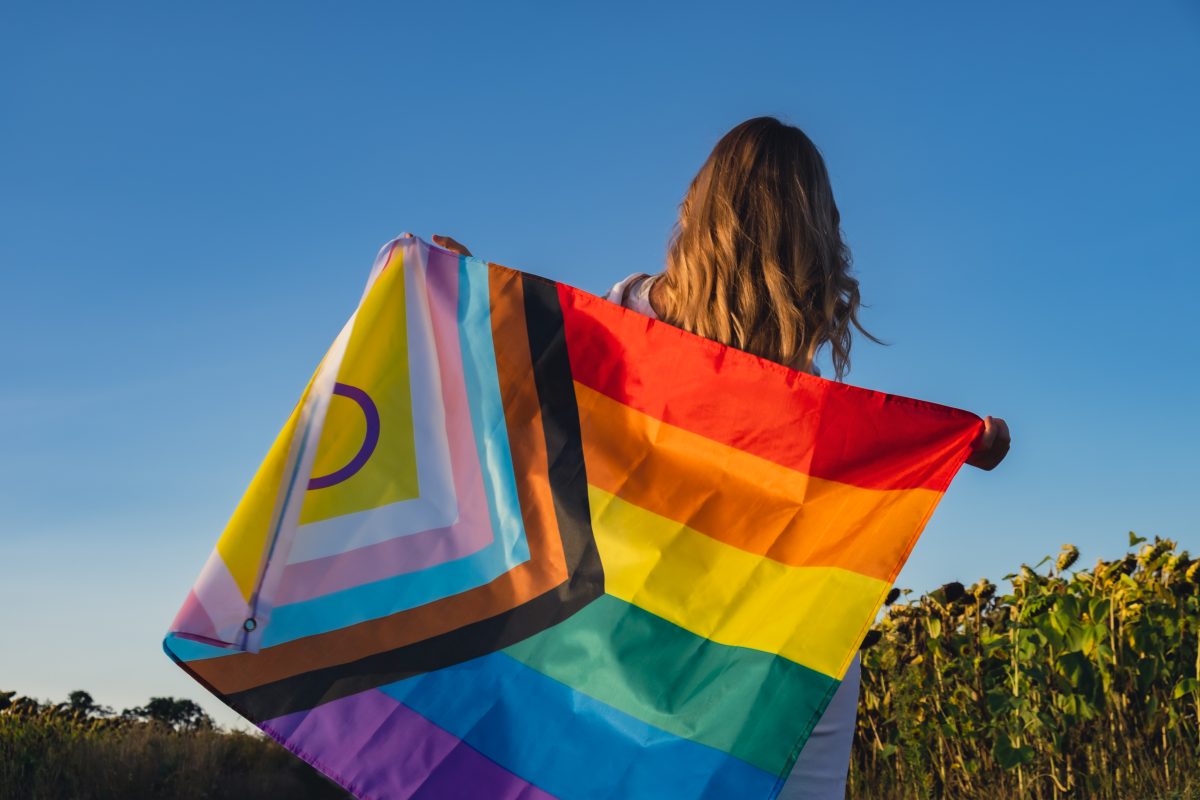 Person photographed from behind holding rainbow Pride flag