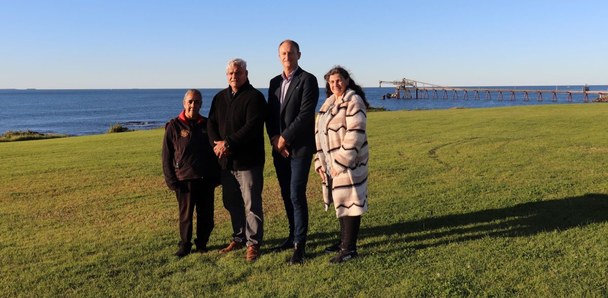 Four people standing together on a hill with ocean in the background