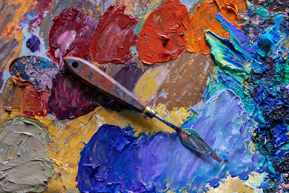 A palette painting knife rests on a palette of different coloured paint on a palette