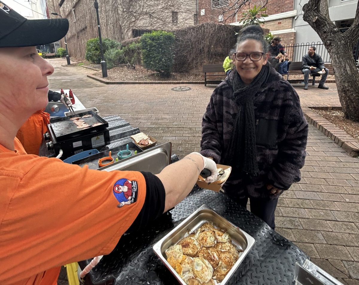 Volunteer assembles a bacon and egg roll for a customer at Need a Feed's breakfast buddies