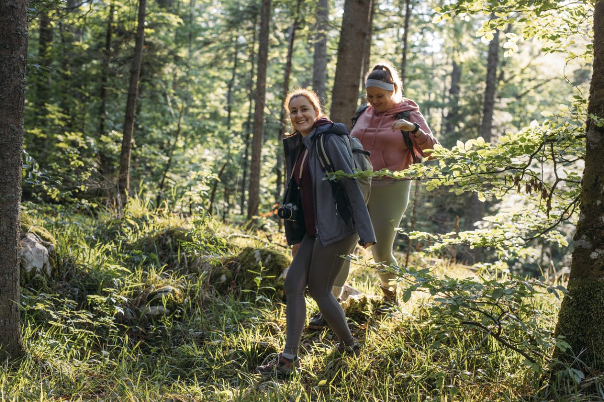 Two smiling women walk through a forest