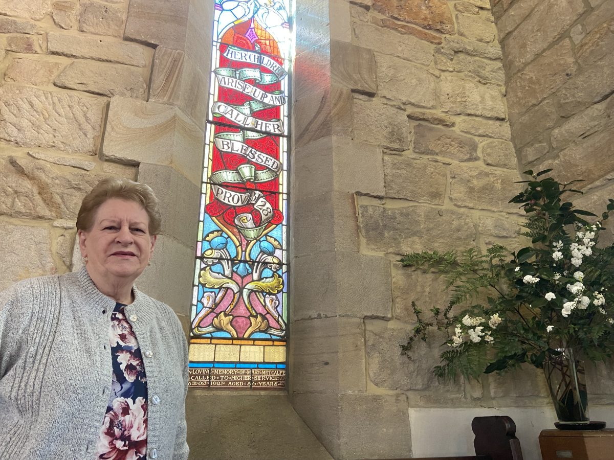 Northern Illawarra Uniting Church member Janice Walker by a leadlight window dedicated to her ancestor Mary Metcalf