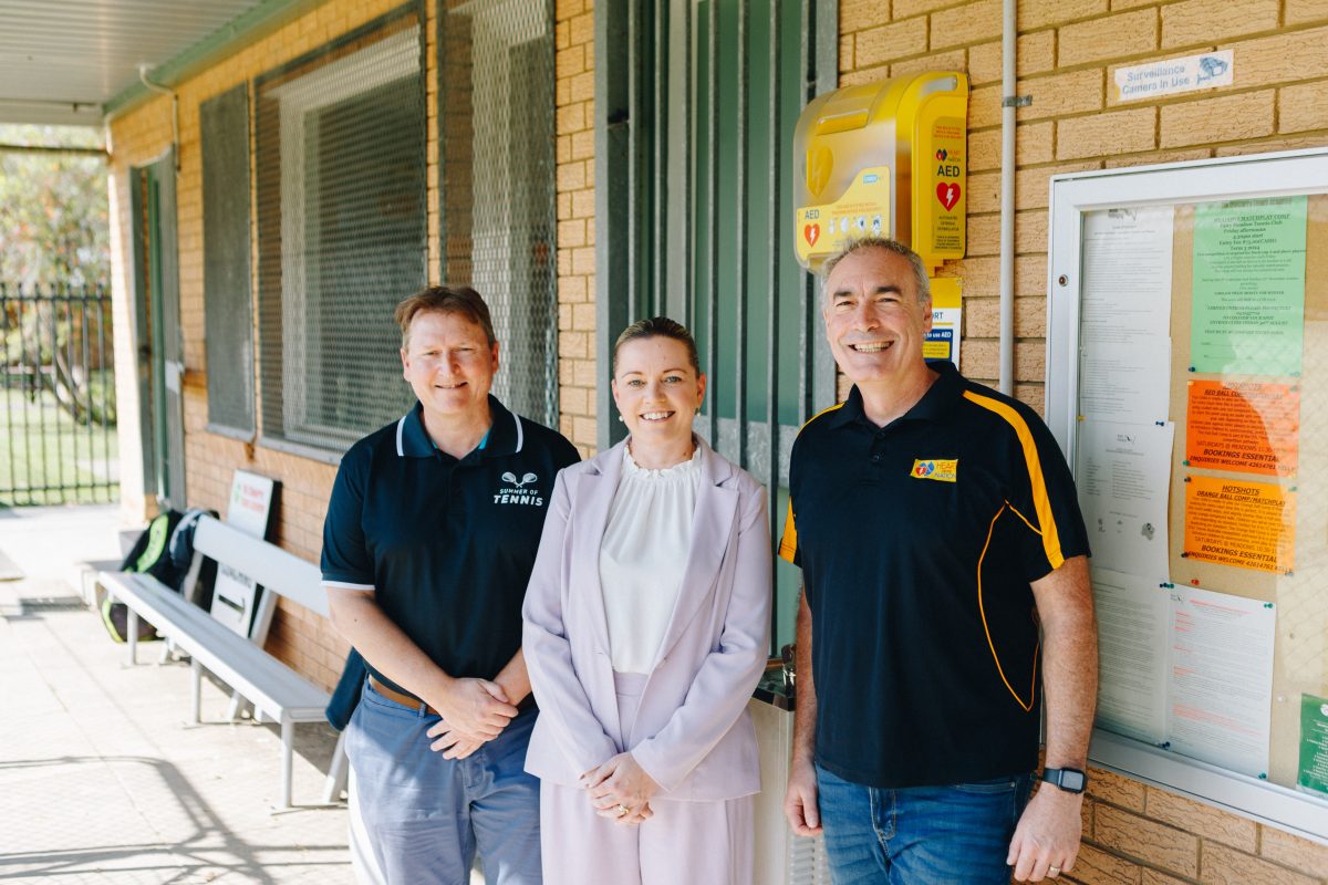 Meadows Tennis Club President David King, Wests Illawarra CFO Renata Garnero and Heart of the Nation CEO and original Yellow Wiggle Greg Page stand in front of an AED at Meadows Tennis Club