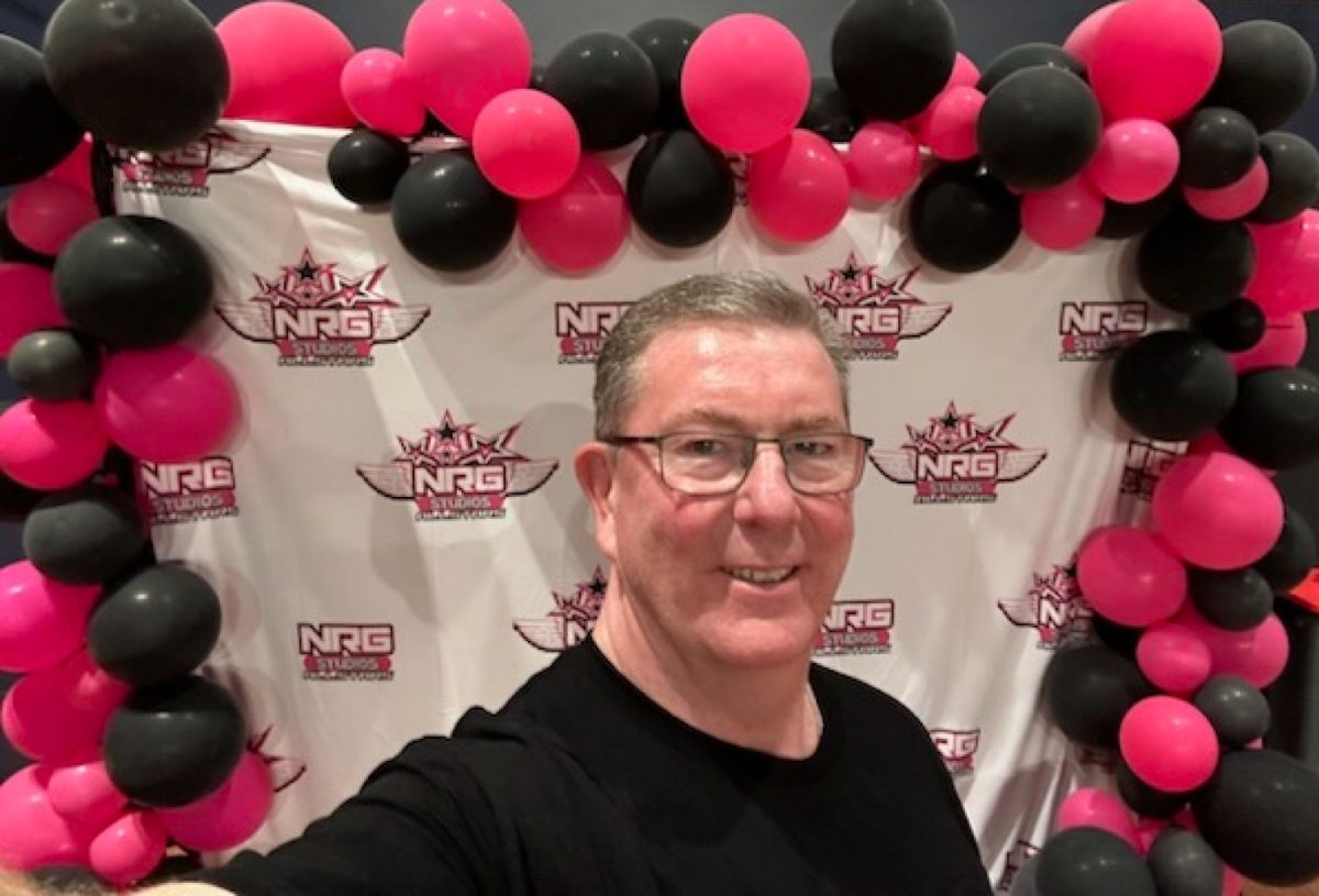 man standing in front of a banner festooned with balloons 