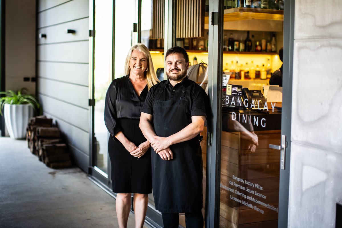 A woman and man both wearing black stand outside a restaurant