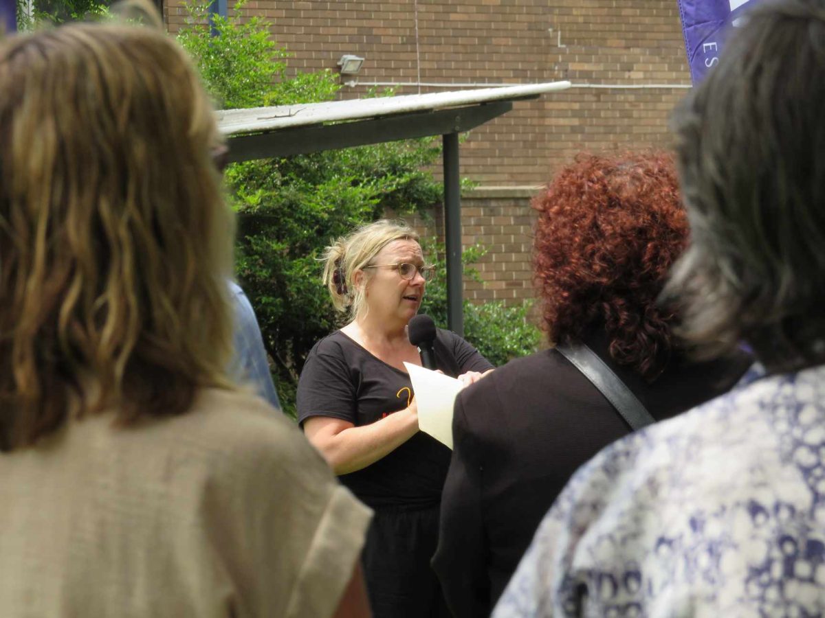 a woman with a microphone addressing a crowd standing outdoors