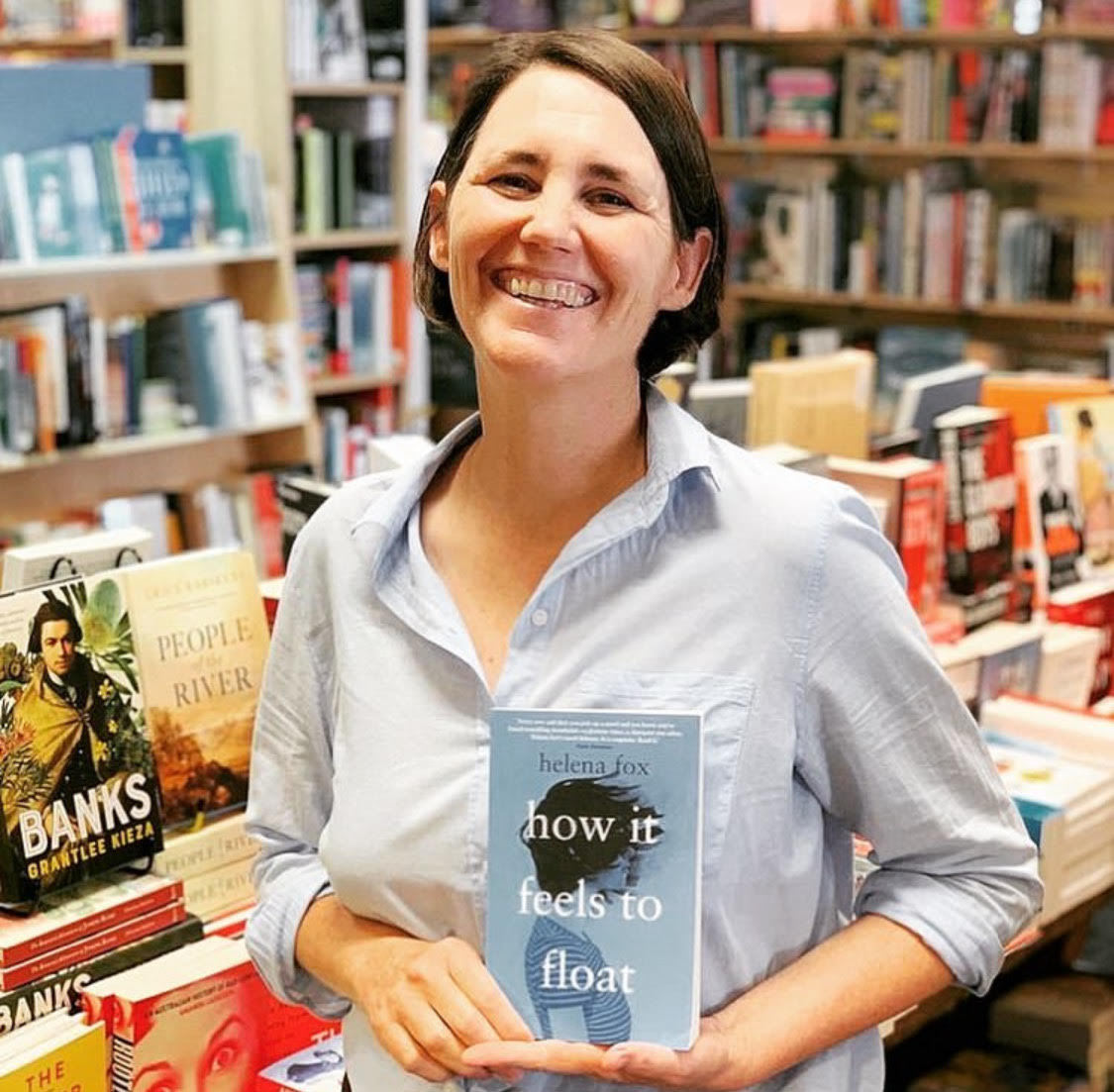 A woman in a bookshop, holding a book she wrote