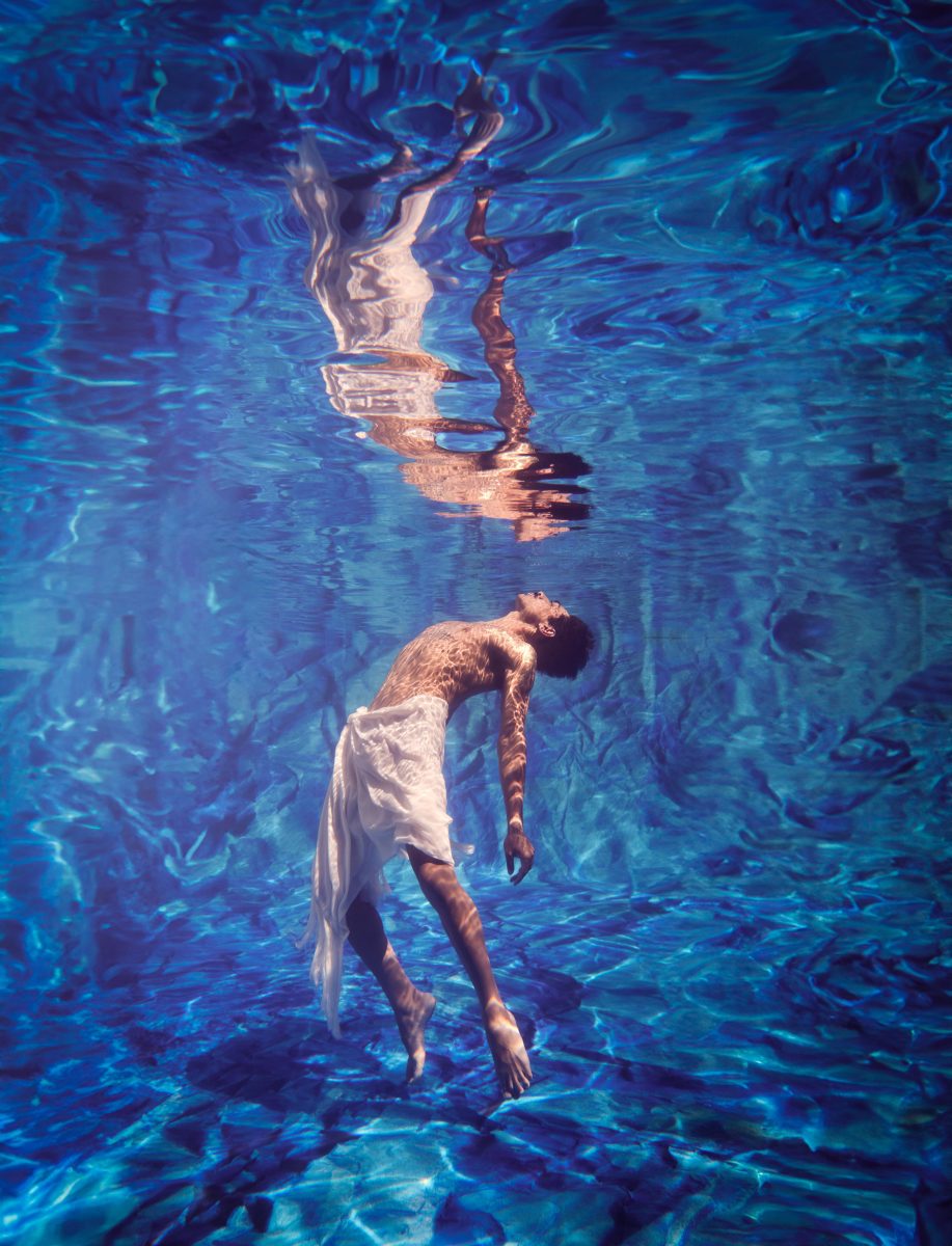 Man floats in blue water and looks up at his reflection