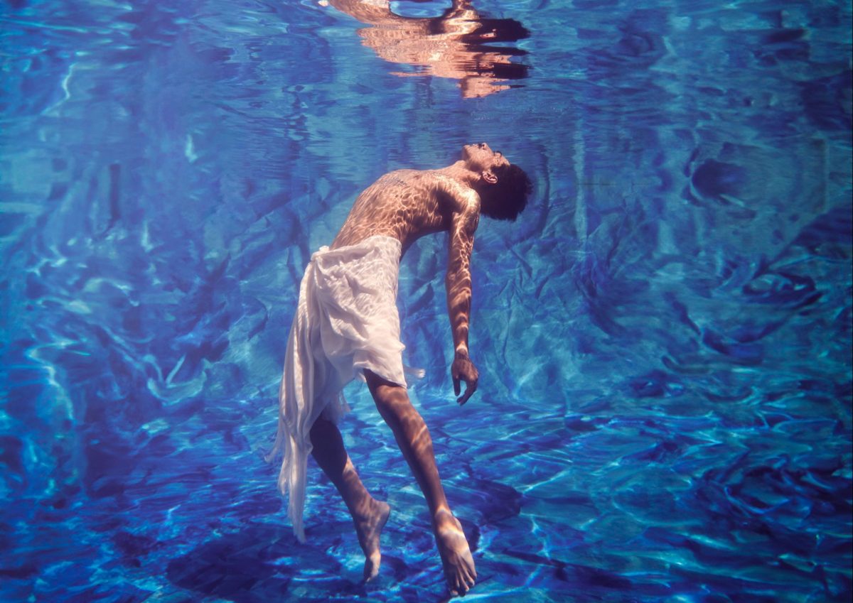 Man floats in blue water and looks up at his reflection