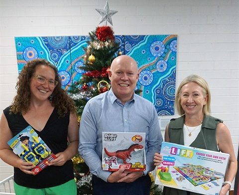 a man and two women holding Christmas gifts in front of a Christmas tree