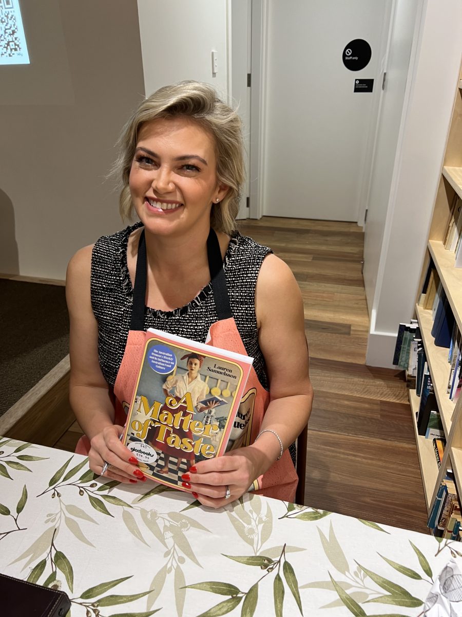 Dr Lauren Samuelsson holding her book, she is wearing a pink apron.