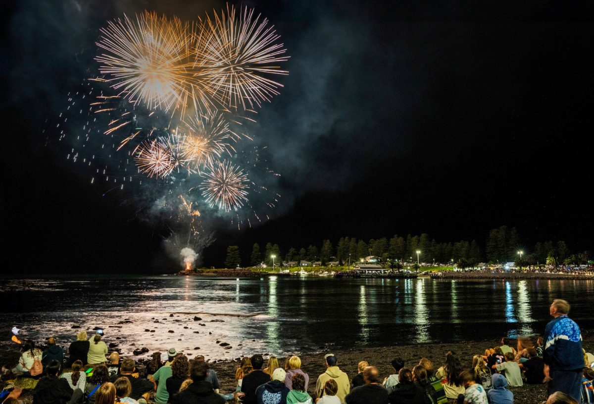 people watching fireworks explode over a harbour