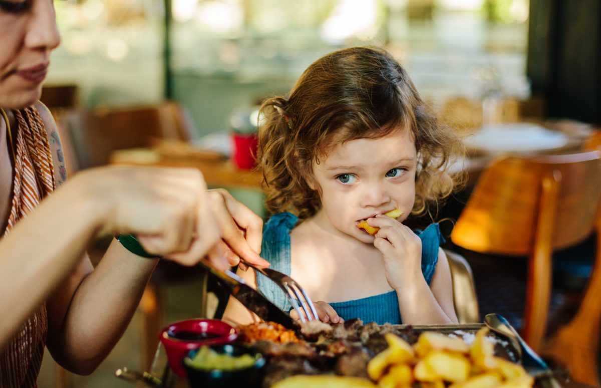 Cute little girl eating her food with her mother's help