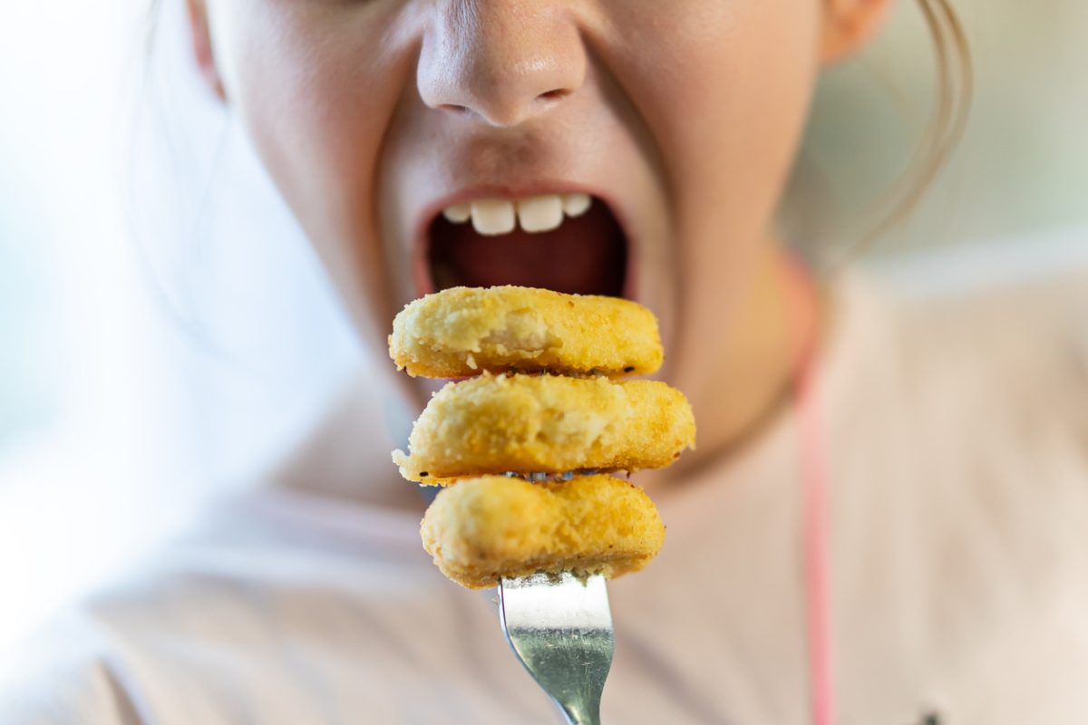 A teenage girl is eating nuggets on a fork. Delicious Chicken nuggets