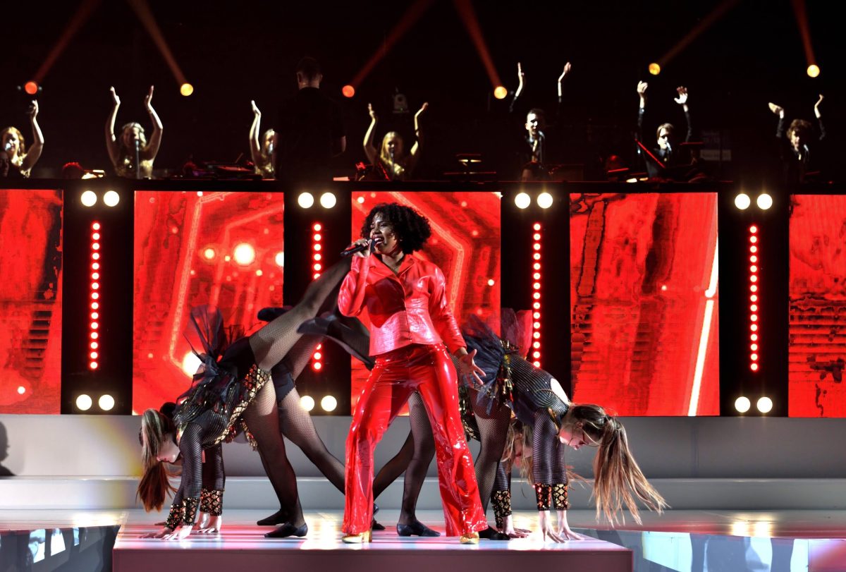 Singer in red on stage with back up dancers