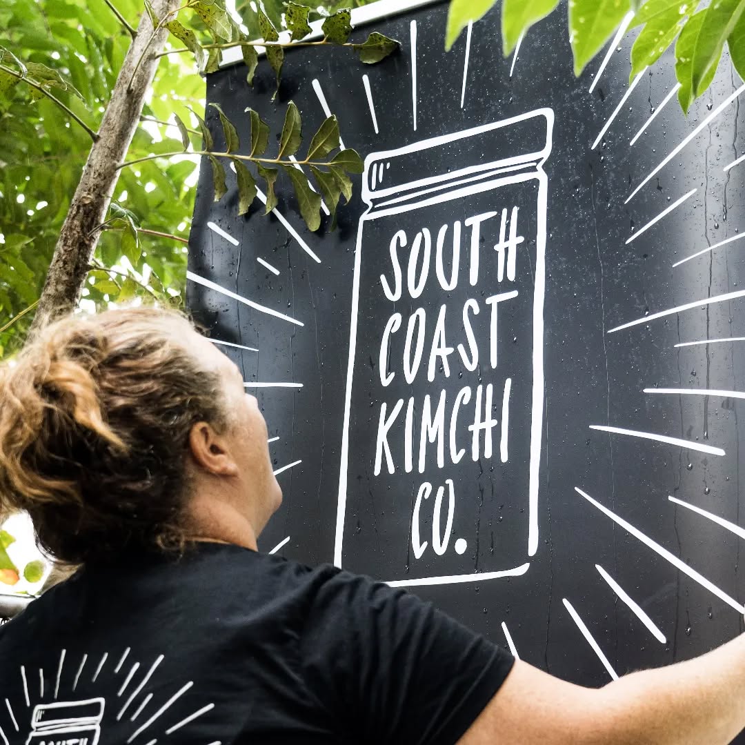 Woman puts up a sign reading South Coast Kimchi Co.