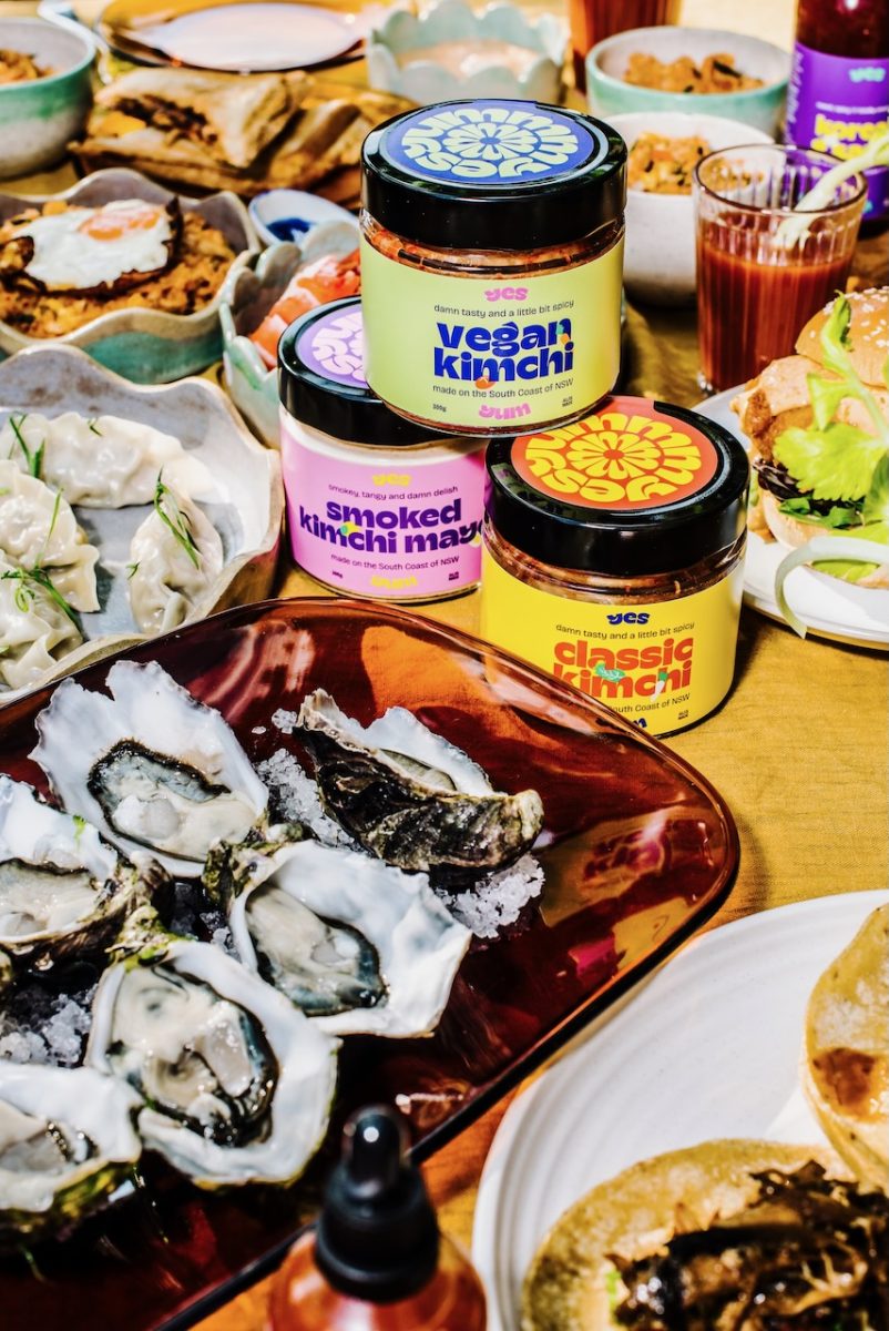 Photo of a busy table with jars of Yes Yum branded products, fresh oysters and other dishes.