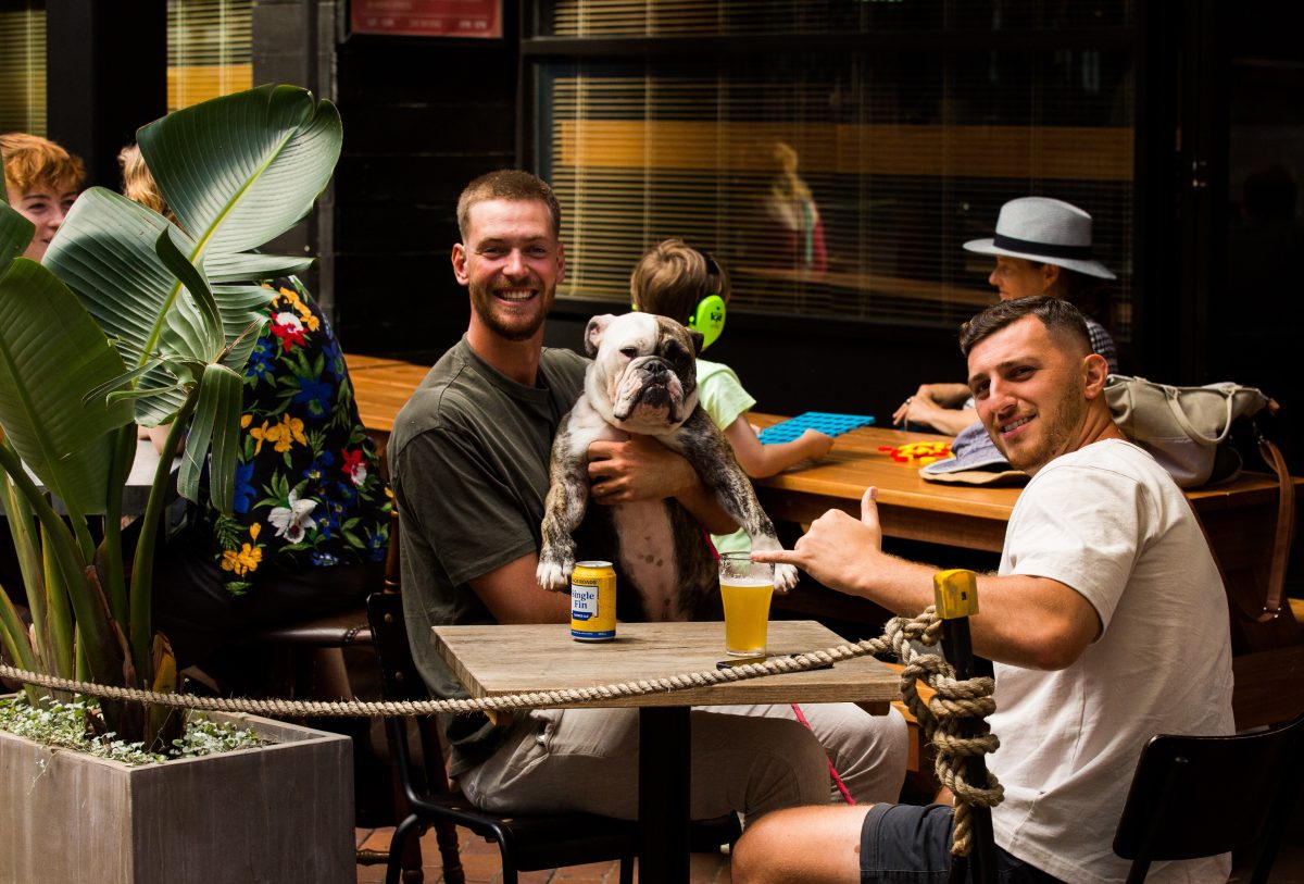 two people and a dog sitting at a table at a bar