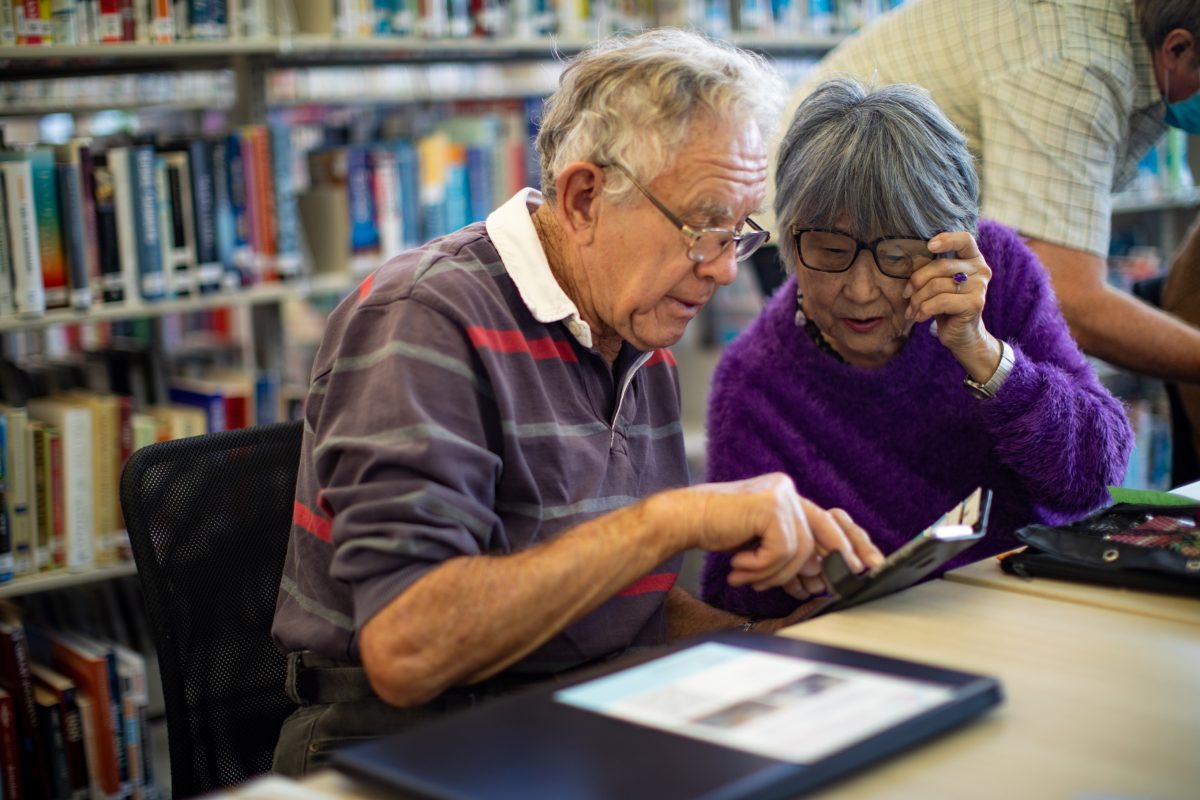 two people looking at a phone sitting at a desk in a library