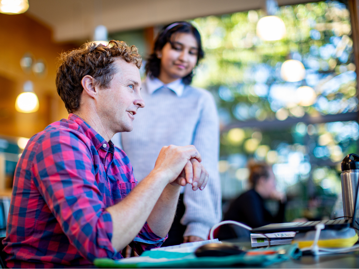 A person sitting at a desk in a library with someone standing next to them