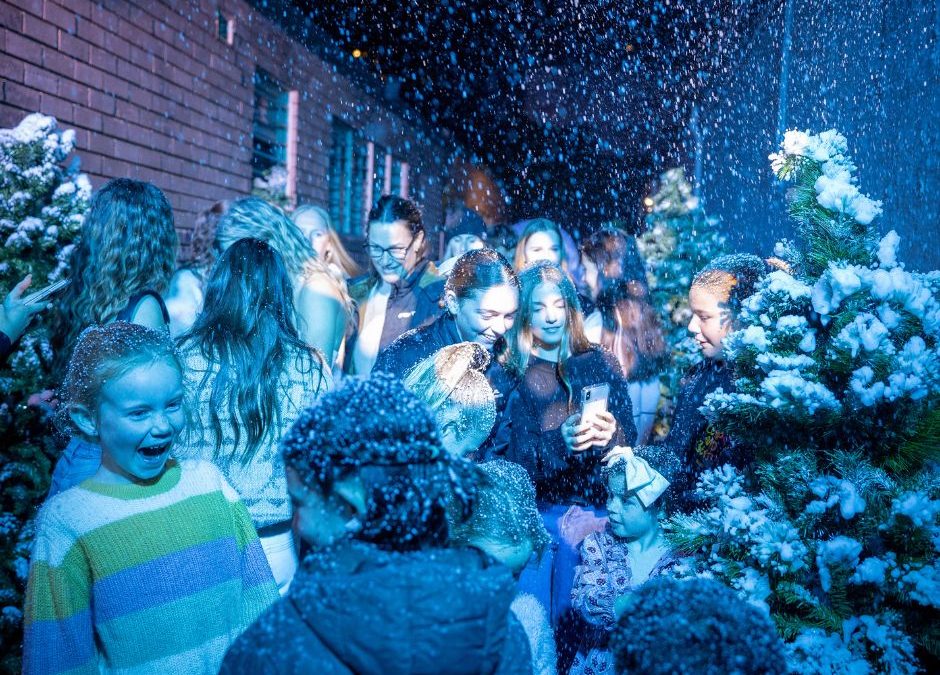 A crowded alley lit blue with artificial snow falling