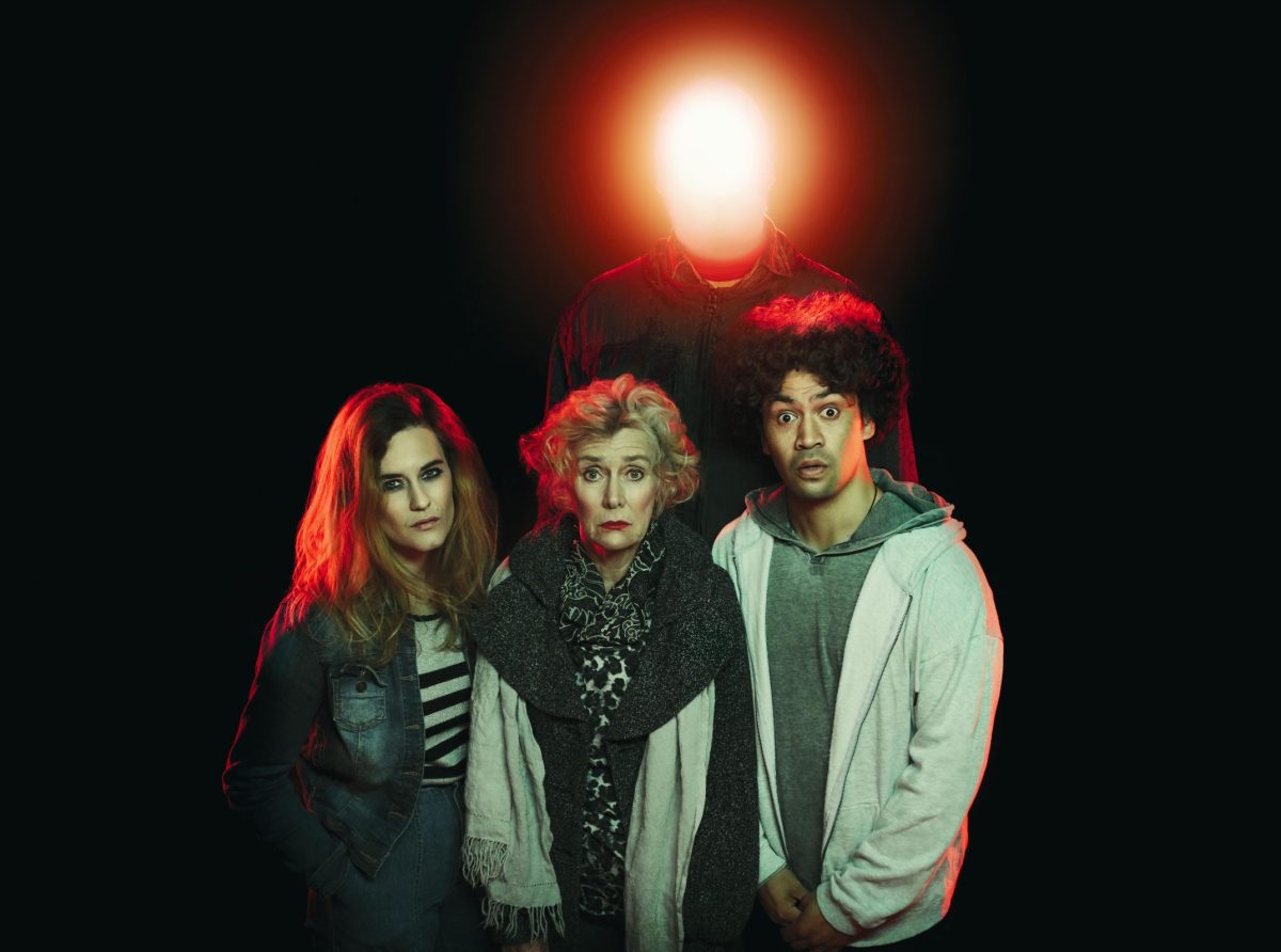 Three people stand in front of a man with a lightbulb head