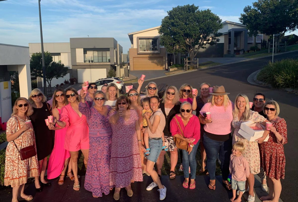 Group of people, many dressed in pink, in the street with wine cups