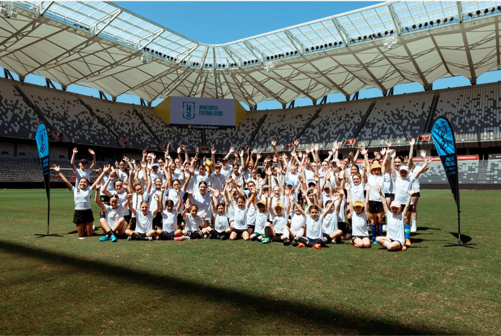 A large group of children poses in a stadium and cheers