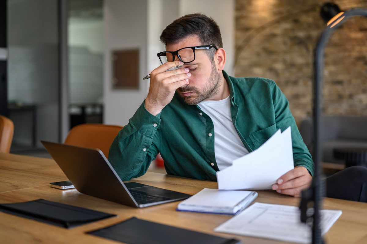 Anxious male rubbing eyes while working over laptop and analysing reports at desk
