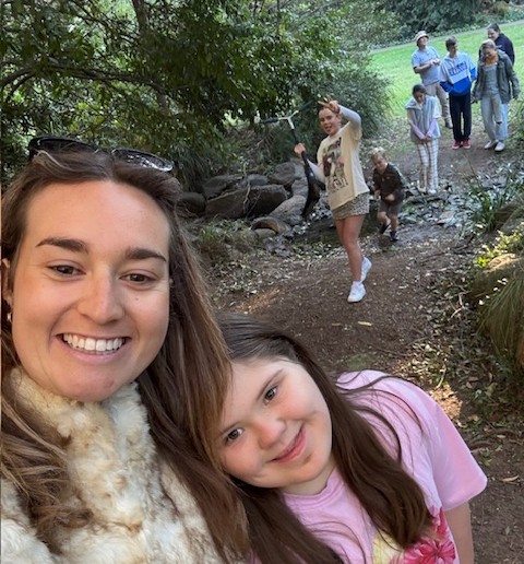 selfie of a woman and a girl outdoors, with people walking behind them