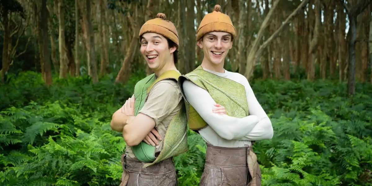 two people dressed in costume as Snugglepot and Cuddlepie standing in front of a forest