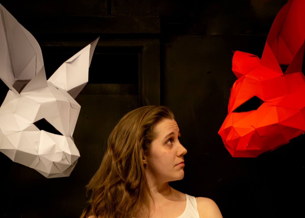 A woman looks at a red rabbit mask and a white rabbit mask is behind her