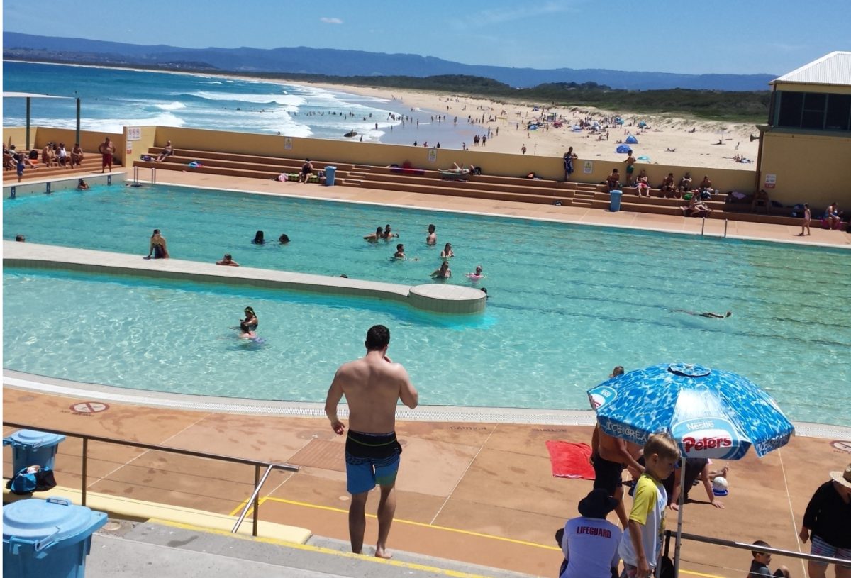 People at a coastal public swimming pool, with a beach in the background