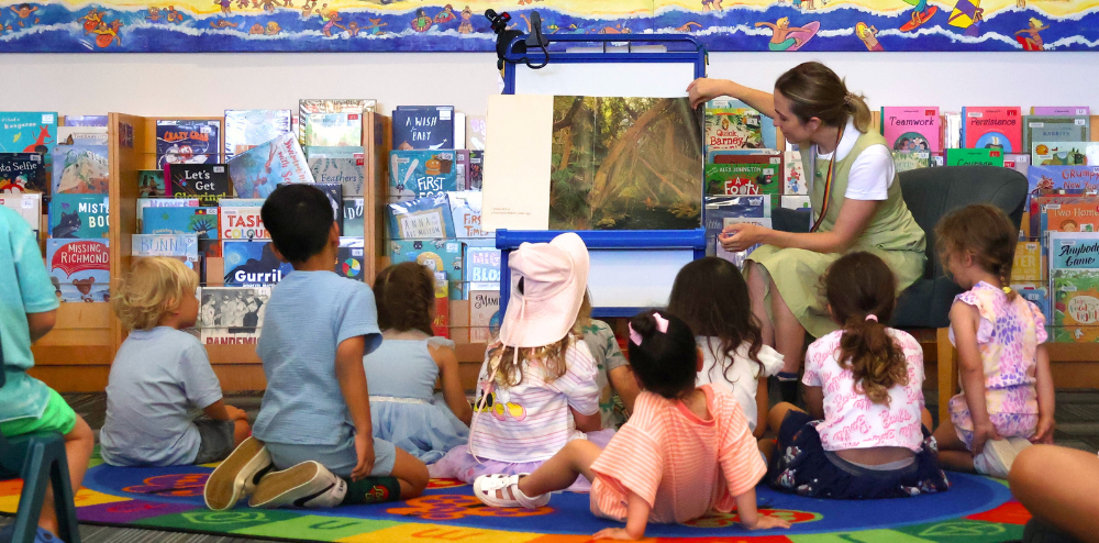 a person reading a book to a group of a children in a library