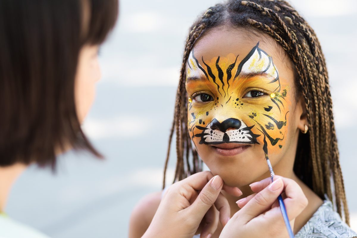 Little girl getting her face painted by face painting artist