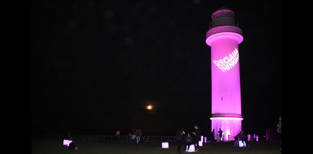 Lighthouse tower lit up in pink with words Reclaim The Night displayed