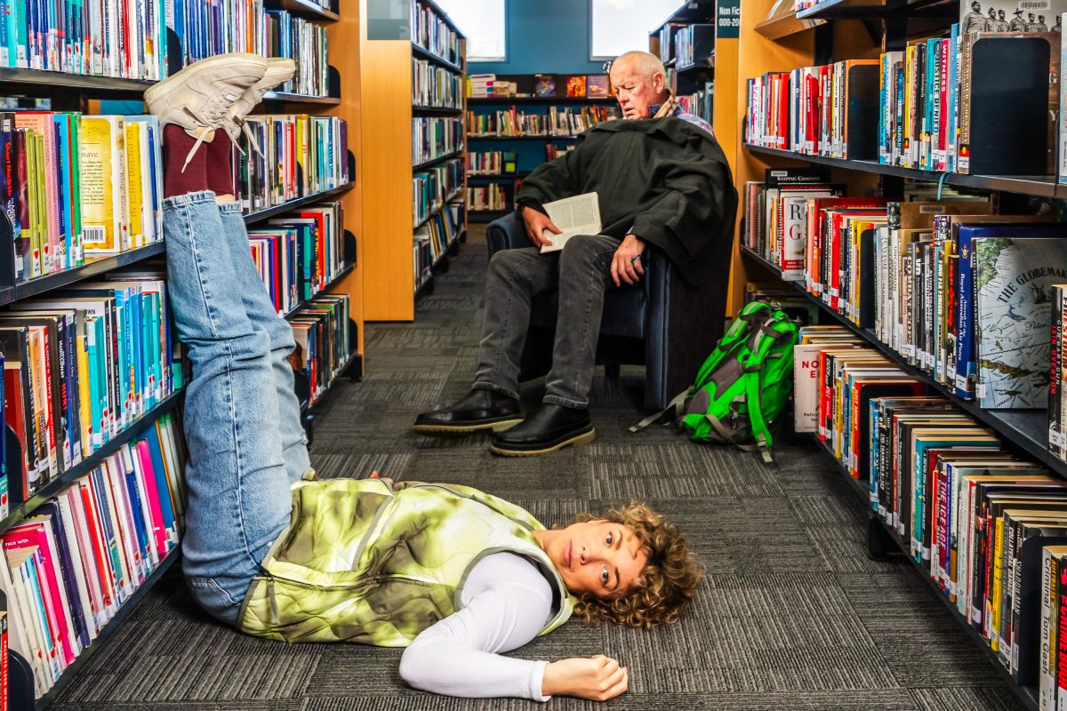 A man sits and reads in the library stacks while a woman lies on the floor