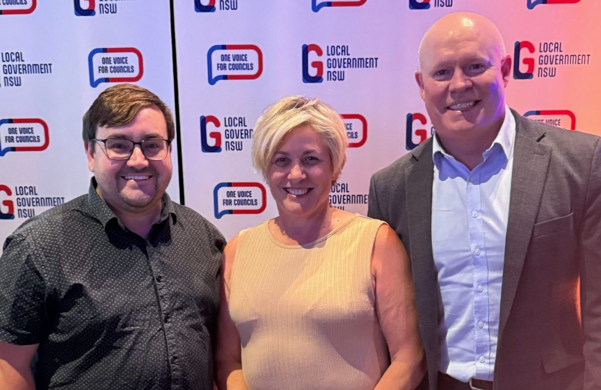 three smiling people standing in front of promotional boards