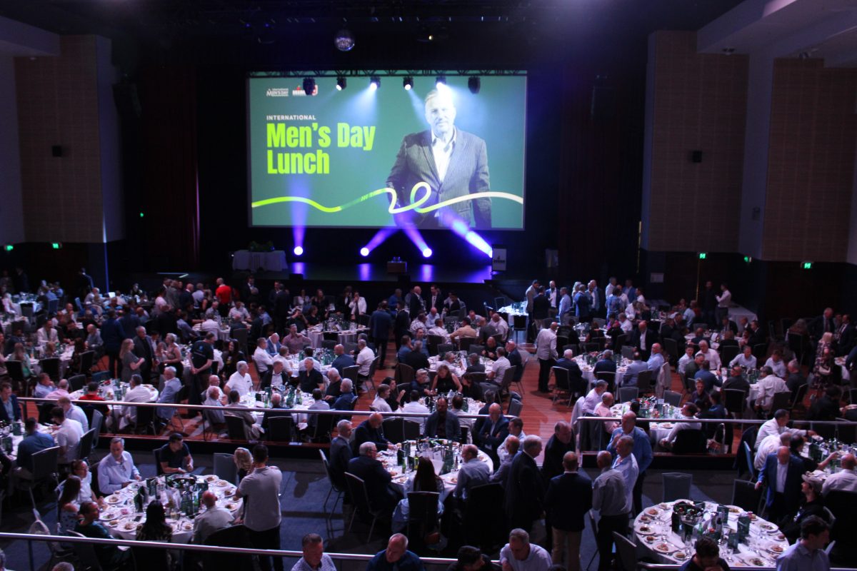 crowd and big screen behind stage at a large lunch gathering in an auditorium