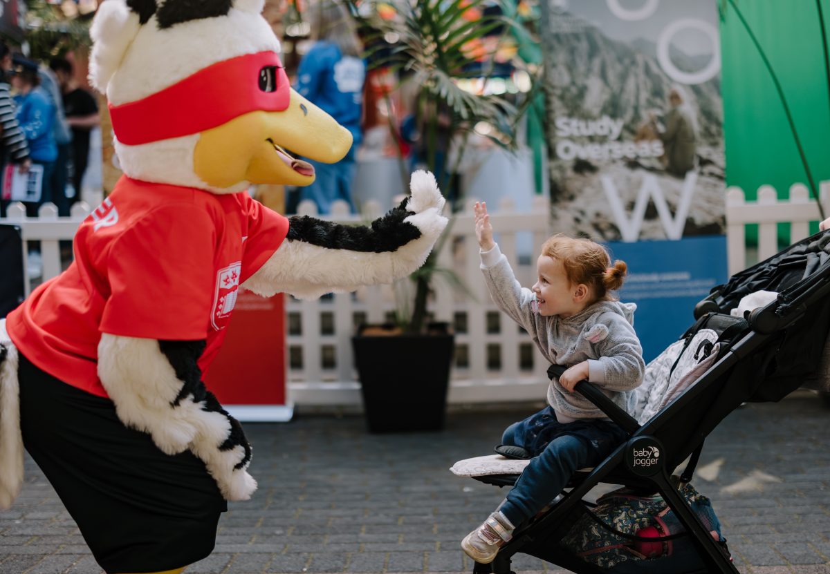 Duck mascot hi fives a child in a pram