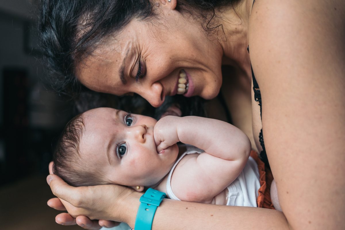 Mother is holding her baby girl and smiling tenderly with love while watching her