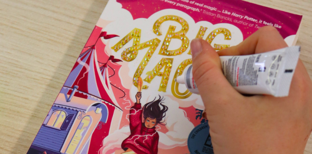 a hand gluing gems onto a book