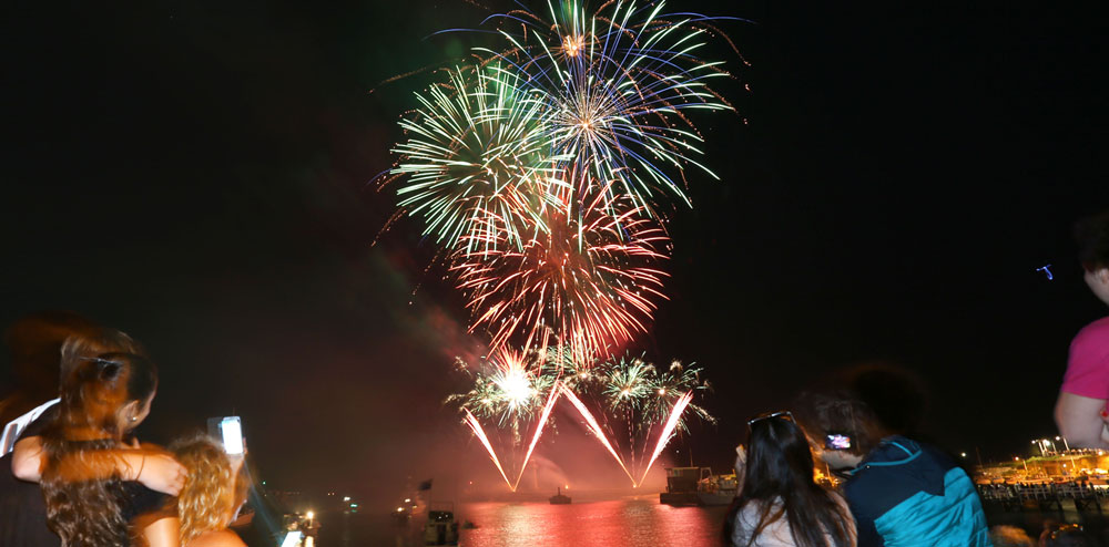 people looking at fireworks over water