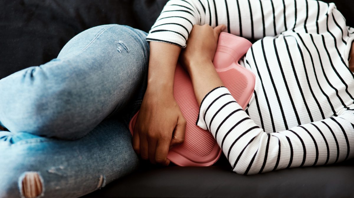 A woman lies on a couch clutching a hot water bottle to her stomach