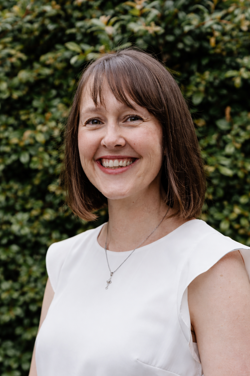 Photo of a woman with brown hair in a white top smiling.
