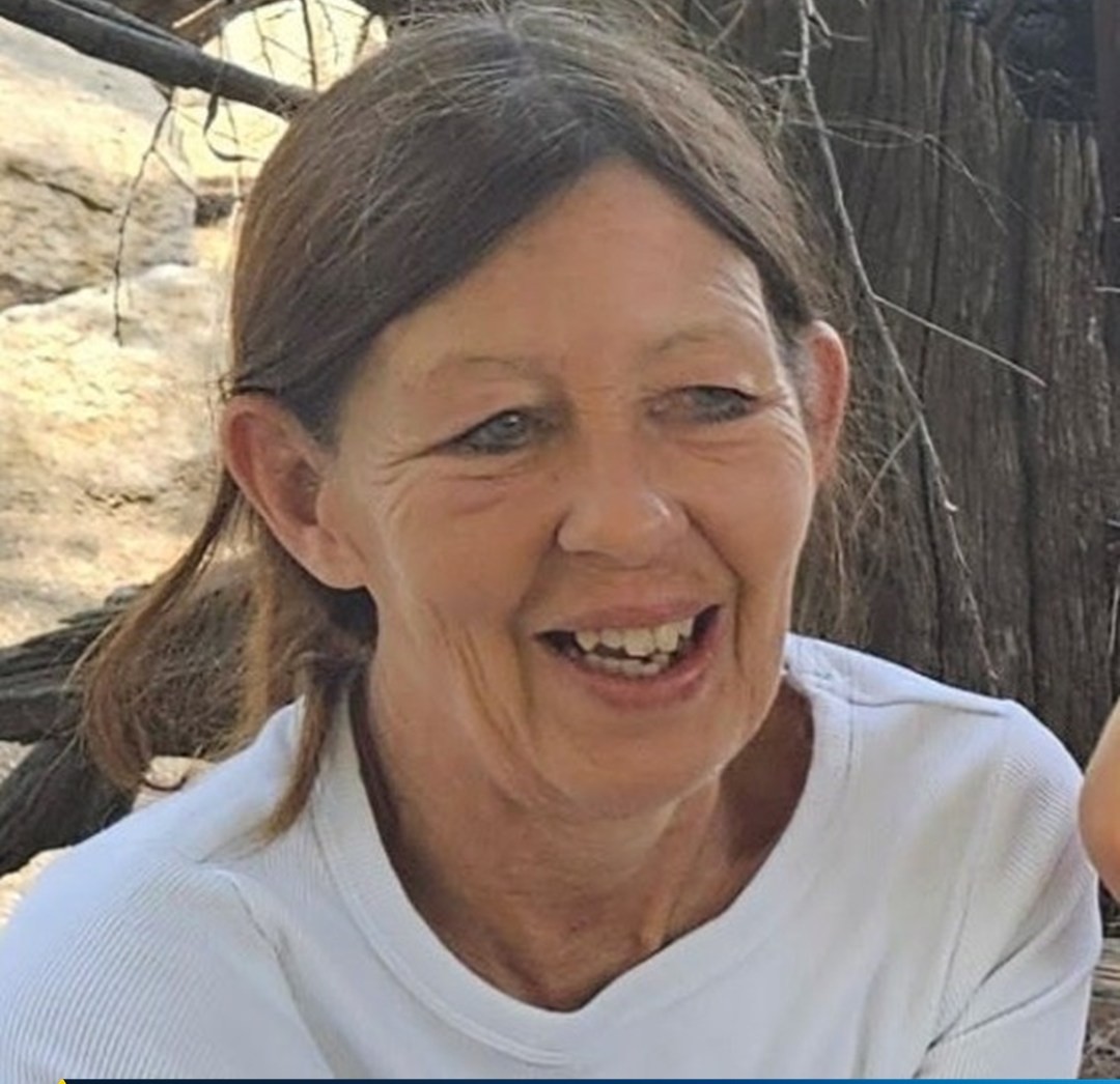 A woman wearing a whit t-shirt with brown hair is smiling.